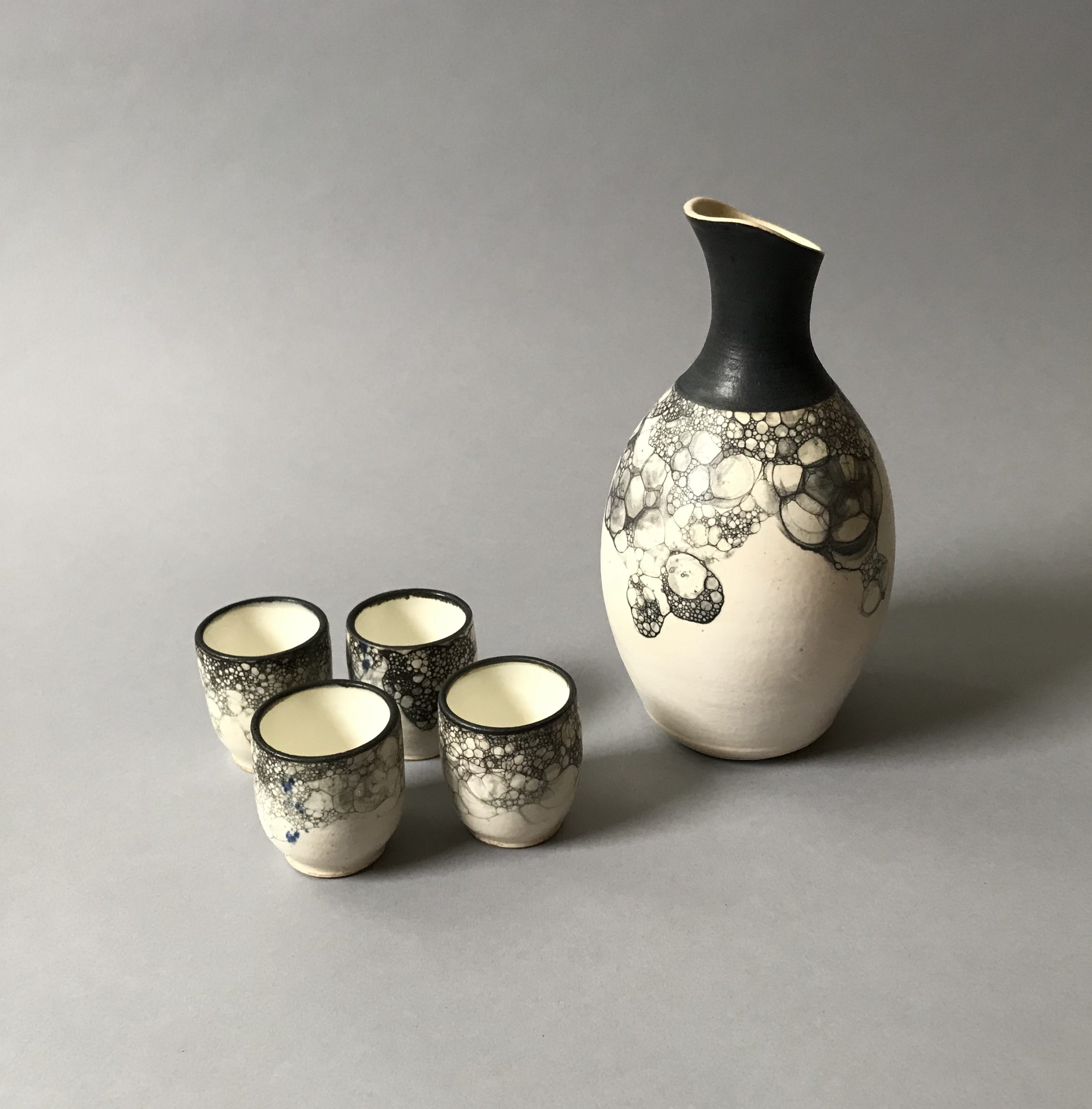 Sake carafe and four large sake cups with black underglaze bubbles on white background